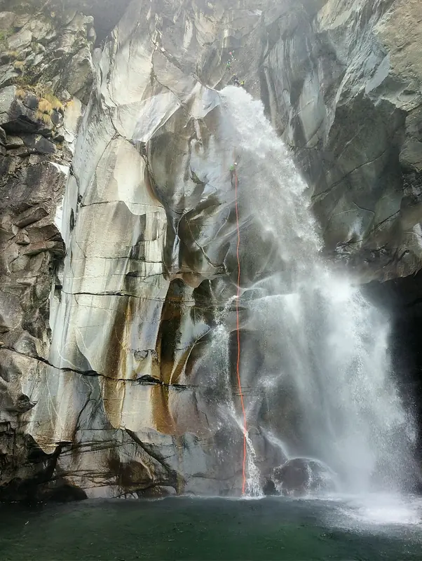 Abseilen am roten Seil neben einem großen Wasserfall im Tessin