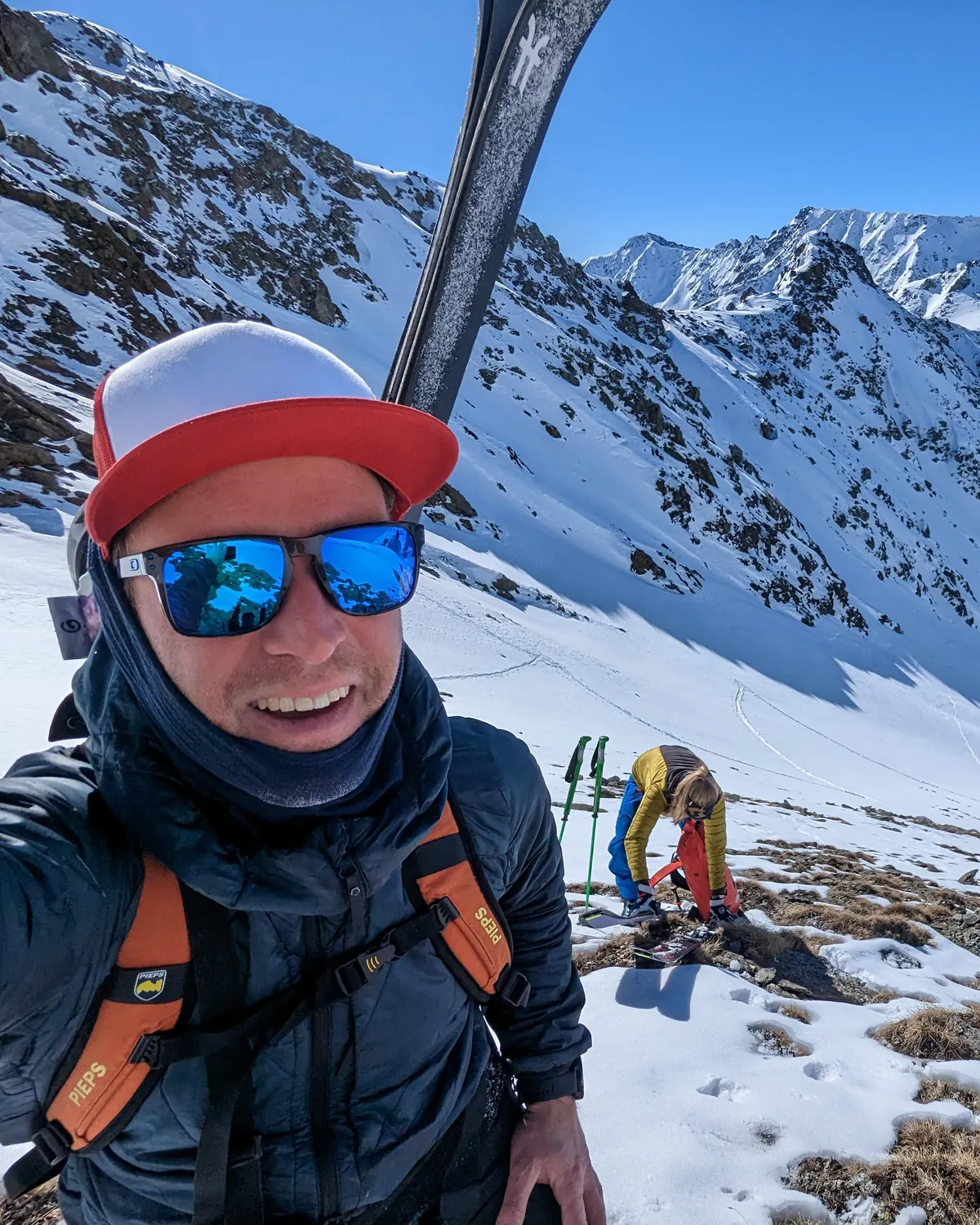 Florian Mihaljevic auf Skitour am Arlberg, Ski auf der Schulter, dahinter verschneite Gipfel